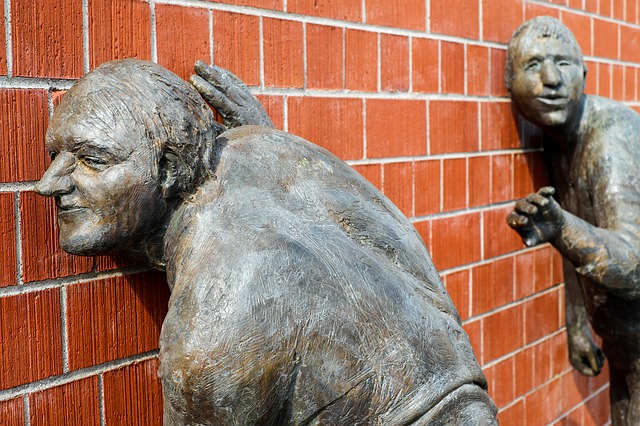 Zwei Bronze-Skulpuren zeigen Männer, die an einer Mauer lauschen