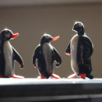 Drei Pinguine aus Glasbläserarbeit stehen nebeneinander und "schauen" auf den Größten mit abgebrochendem Schnabel