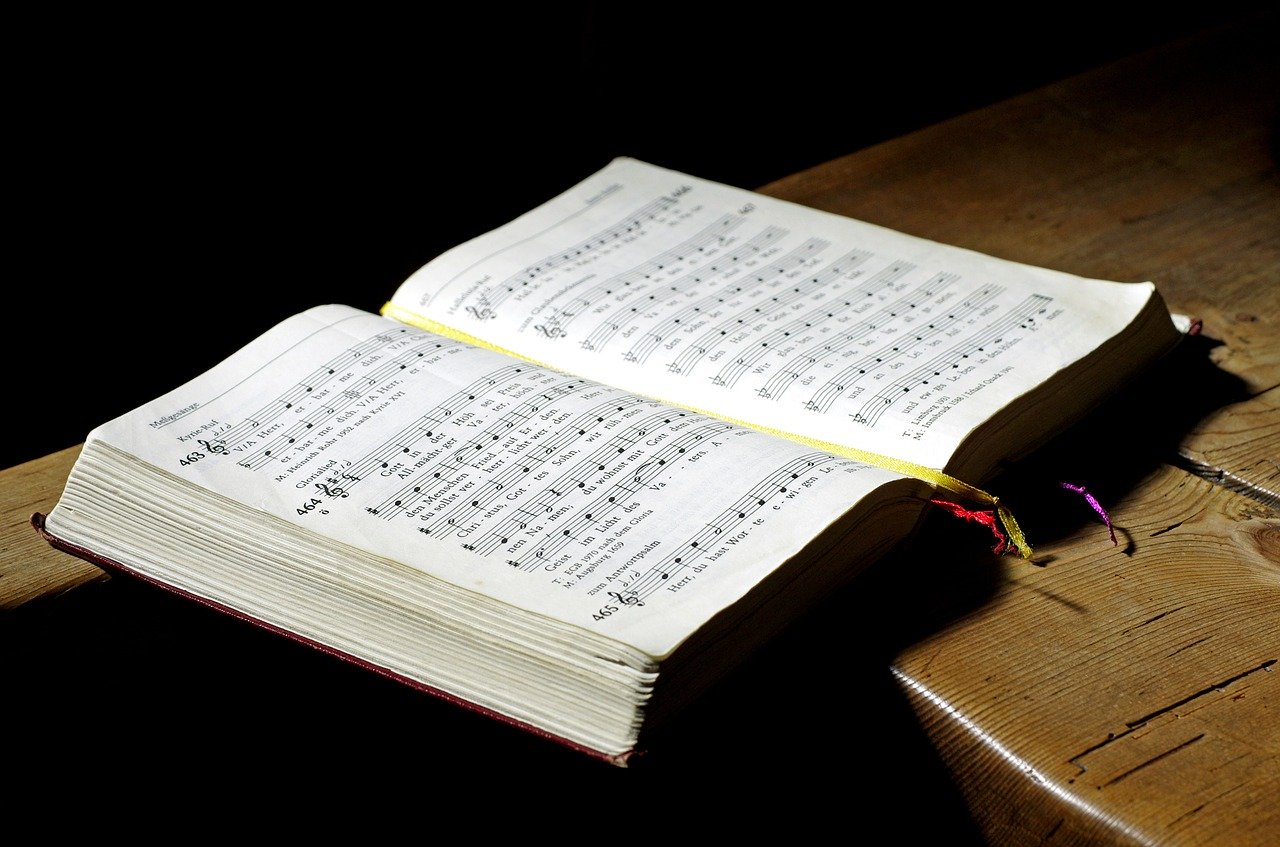Ein Gesangbuch liegt aufgeschlagen auf einem markanten Holztisch. Licht fällt auf Buch und Tisch.
