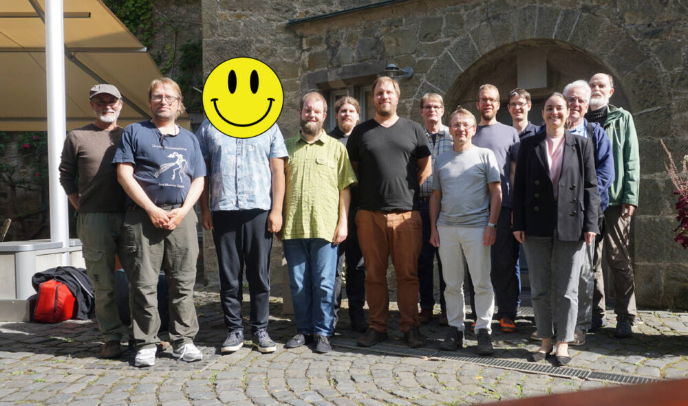 Gruppenfoto der Teilnehmer im Hof der Burg. Sie stehen vor dem Eingangsportal. Es ist ein alte Steinmauer mit Rundbogentür Das Gesicht eines Teilnehmers ist mit einem Smiley versehen..